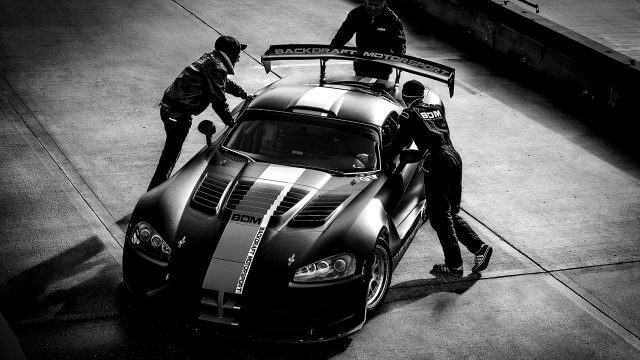 Black and White Image of racing car with crew in pit lane